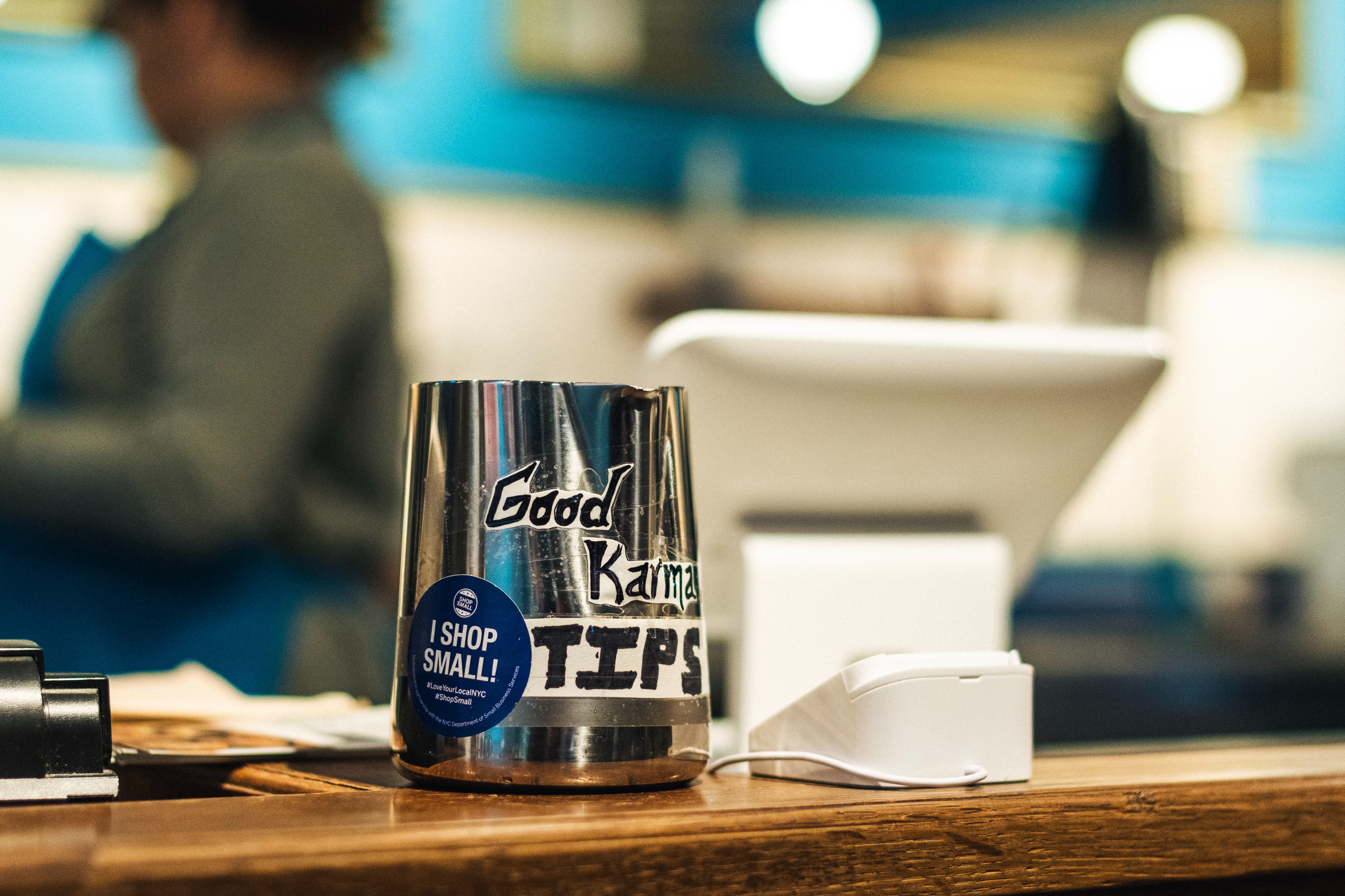 Tip jar that reads 'Good Karma Tips' on a ledge beside a new tipping machine, with a tablet for ordering in the background. 