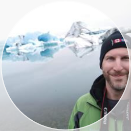 Trevor Smith smiles at the camera, standing in front of glaciers.