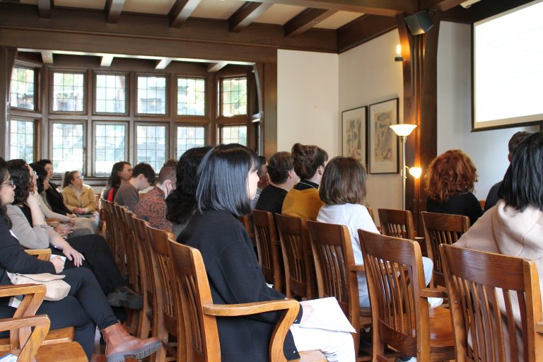 Group of people sitting in rows of wooden chairs at Green College's Coach House, listening to a presentation.