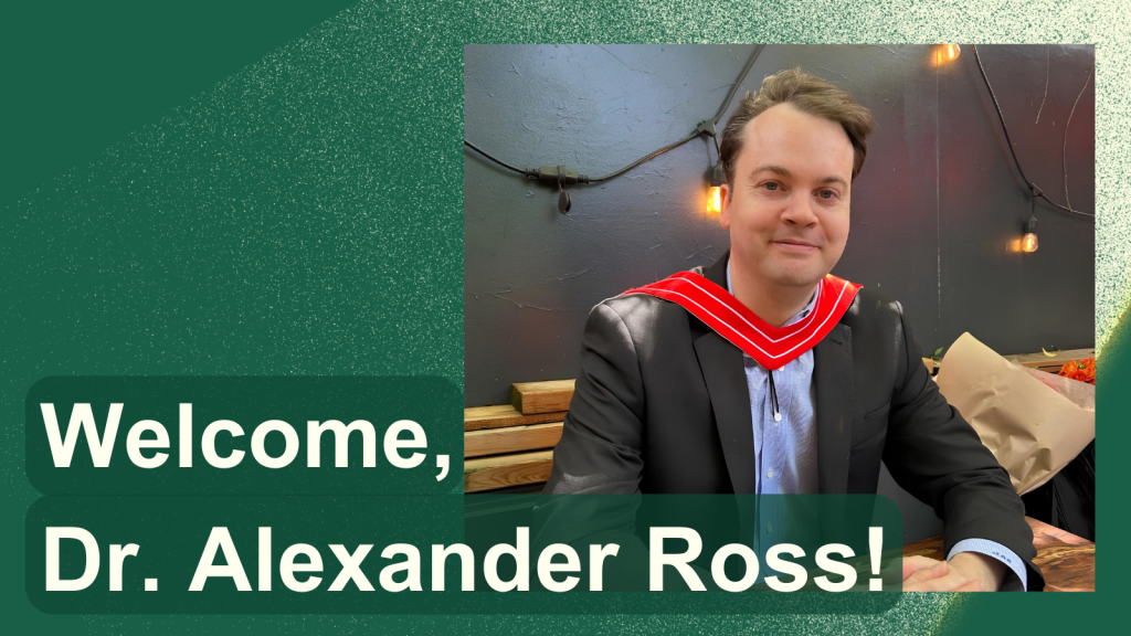 Welcome, Dr. Alexander Ross! Dr. Alexander Ross is wearing a dark grey suit and light blue button up, with a red graduation sash. He is sitting at a table with his arms resting on the table, smiling at the camera.