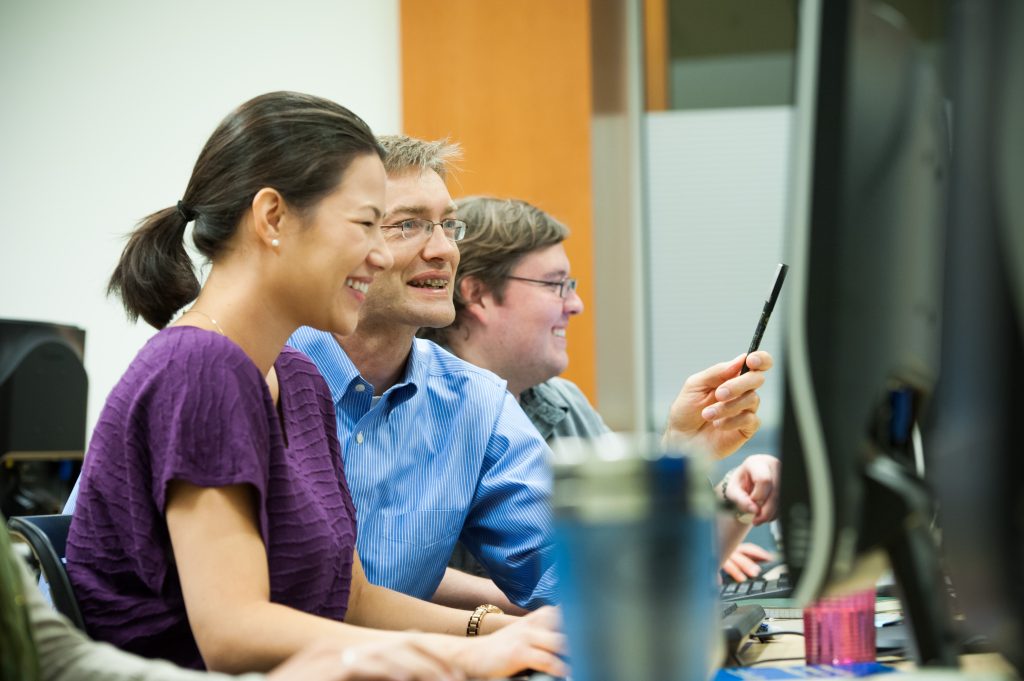 Dr. Eric Meyers sits with two students in the computer lab, looking at the computer screens with smiles.